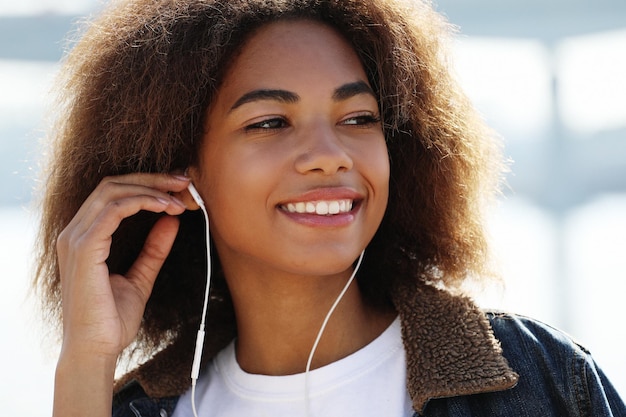 Conceito de estilo de vida Jovem afro-americana usando telefone celular e fones de ouvido sorrindo