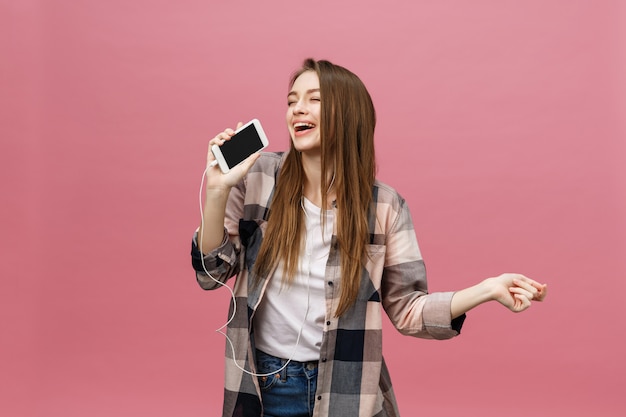 Conceito de estilo de vida. jovem mulher usando telefone para ouvir música no fundo rosa