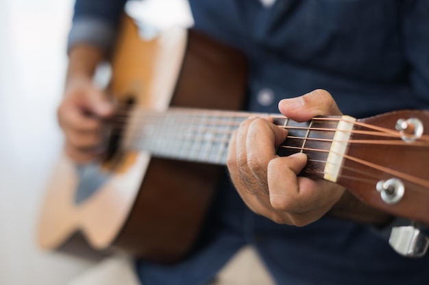 Foto conceito de estilo de vida. jovem músico asiático tocando violão na sala de estar em casa neste fim de semana. relaxando com música e música. homem asiático se divertindo tocando violão