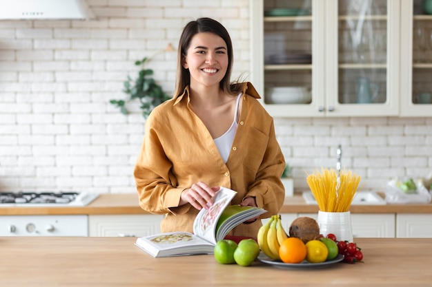 Conceito de estilo de vida saudável. Mulher jovem e bonita com um conjunto de alimentos para nutrição saudável fica em casa na cozinha