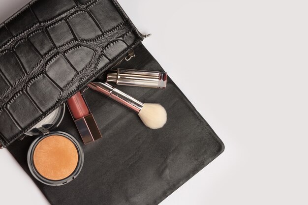 Conceito de estilo mulher: bolsa de couro feminina com bronzeador, pincel e batom sobre um fundo cinza. Espaço vazio