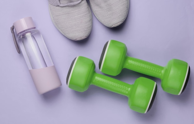 Conceito de estilo plano leigo de esporte de estilo de vida saudável e fitness Sapatos esportivos para correr halteres garrafa de água no fundo roxo pastel Vista superior
