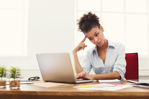 Conceito de estresse de prazo - triste mulher de negócios afro-americanos sentada na área de trabalho no escritório e segurando a mão na cabeça. Um duro dia de trabalho.