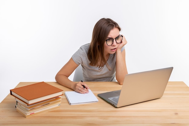 Conceito de estudante e educação - jovem pensativa sentada à mesa de madeira com o laptop