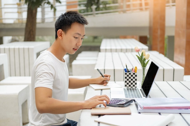 Conceito de estudo on-line um estudante do sexo masculino em camiseta branca estudando on-line usando seu novo laptop branco