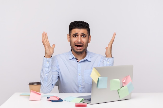 Conceito de excesso de trabalho de horas extras Empregado de homem assustado chocado sentado no local de trabalho do escritório levantando as mãos gritando com medo notas pegajosas ao redor lembrando do prazo tiro de estúdio interno isolado