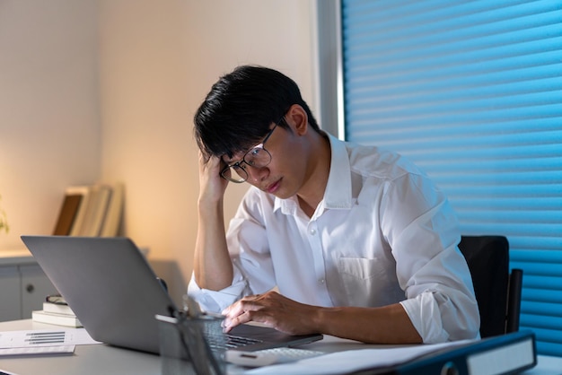 Conceito de excesso de trabalho O oficial masculino descansando a testa na mão direita enquanto trabalhava até tarde