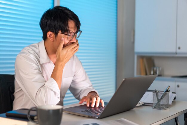 Conceito de excesso de trabalho o pessoal do escritório na gravata solta sentado em sua mesa lendo uma papelada e digitando no notebook