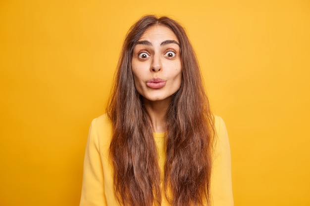 Conceito de expressões do rosto humano. Mulher bonita surpresa com longos cabelos escuros mantendo os lábios dobrados