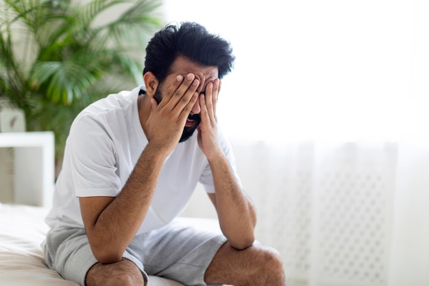 Conceito de fadiga cansado jovem indiano sentado na cama e esfregando os olhos