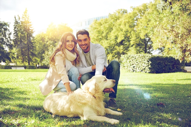 conceito de família, animal de estimação, animal e pessoas - casal feliz com cachorro labrador retriever andando no parque da cidade