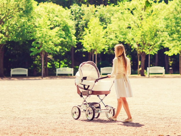 Conceito de família, criança e paternidade - mãe feliz andando com o carrinho de bebê no parque de volta