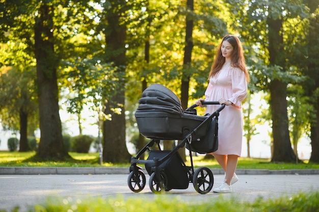 Conceito de família, criança e paternidade - mãe feliz andando com o carrinho de bebê no parque.