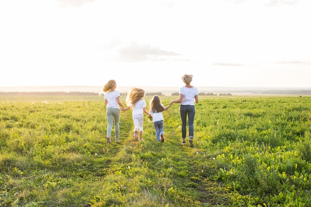 Conceito de família, diversão e férias - mães e suas filhas indo embora em campo verde.