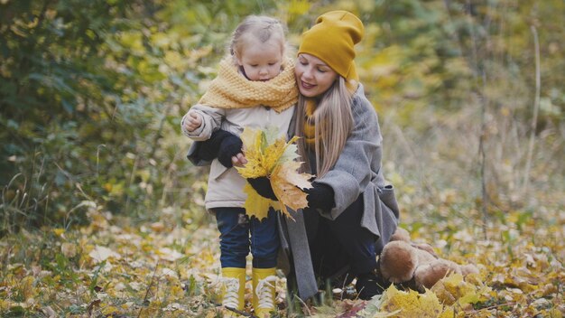 Conceito de família feliz - linda filhinha com a mãe brinca com folhas amarelas no parque outono, telefoto