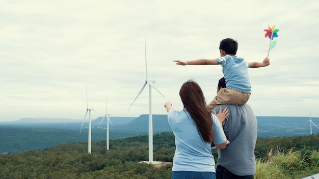 Conceito de família feliz progressiva desfrutando de seu tempo na fazenda de turbinas eólicas Gerador elétrico a partir do vento por gerador de turbinas eólicas no lado do campo com colina e montanha no horizonte