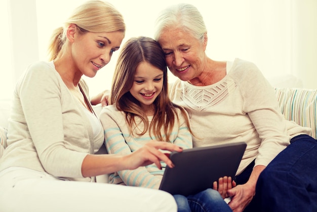 conceito de família, geração, tecnologia e pessoas - sorrindo mãe, filha e avó com computador tablet pc sentado no sofá em casa