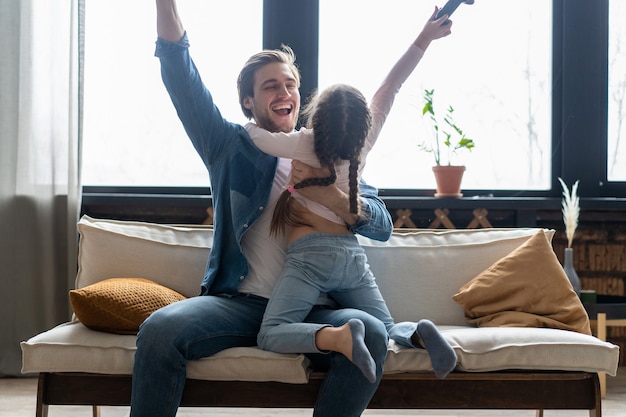 Conceito de família, jogos e entretenimento - feliz pai e filha com gamepads jogando videogame em casa.