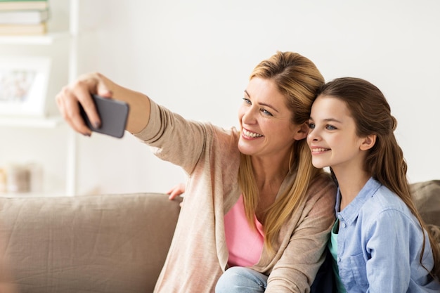 Foto conceito de família, tecnologia e pessoas - feliz mãe e filha com smartphone tirando selfie em casa