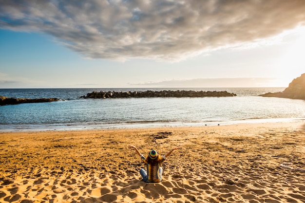 Foto conceito de felicidade com visão traseira de uma jovem sentada na praia e abraçando o oceano e a natureza à sua frente