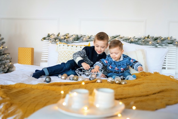 Conceito de felicidade de natal, natal, ano novo - crianças sorridentes com muitos brinquedos de natal. meninos brincando com bolas de natal e sorrindo na cama. irmãos mais novos felizes celebrando o natal.