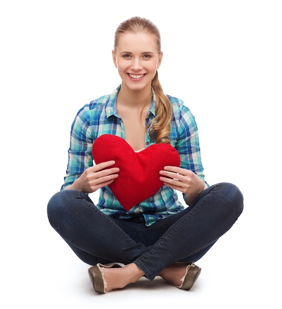 conceito de felicidade e pessoas - jovem sorridente em roupas casuais sentada no chão e segurando coração vermelho