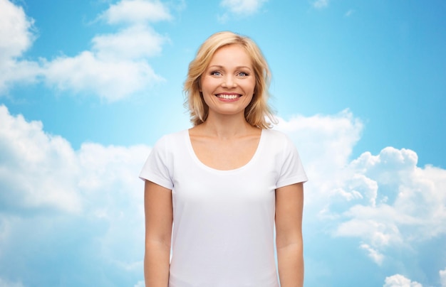 conceito de felicidade e pessoas - mulher sorridente em t-shirt branca em branco sobre o fundo do céu azul e nuvens