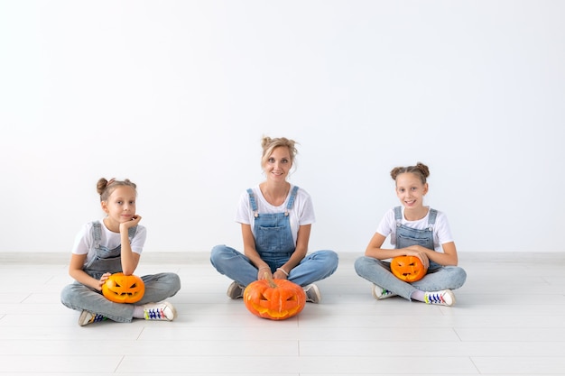 Conceito de feliz dia das bruxas e feriados - uma mãe e suas filhas com abóboras. família feliz se preparando para o halloween.