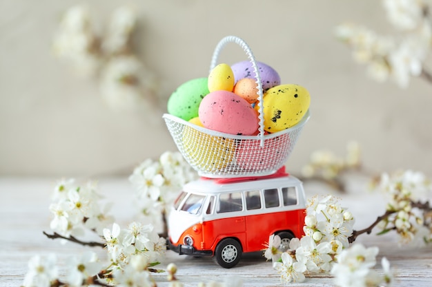 Conceito de feriado da páscoa - carrinho de brinquedo carregando ovos de páscoa coloridos em uma cesta durante o período de floração
