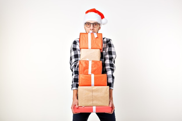 Conceito de feriados e presentes - homem engraçado com chapéu de natal segurando muitas caixas de presente em um fundo branco com copyspace