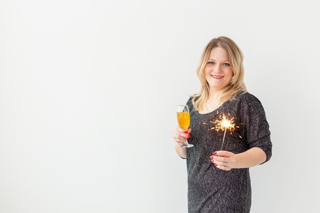 Conceito de feriados, natal, aniversário e ano novo - mulher comemora e segura o vinho em uma taça e espumante sobre fundo branco, close-up