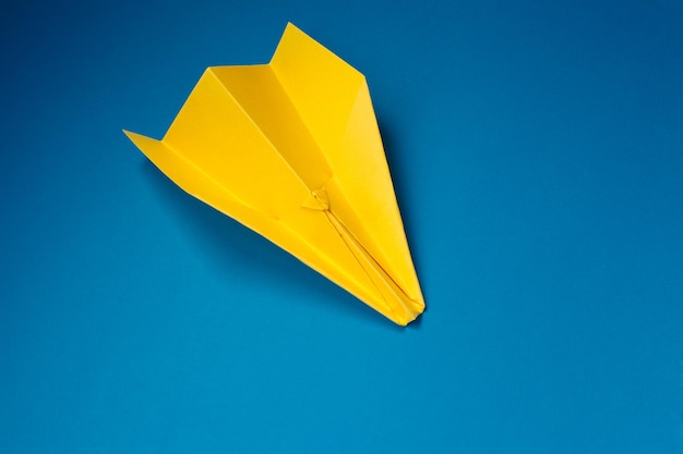 Foto conceito de feriados, tradição, estilo e minimalismo - avião de origami amarelo sobre fundo azul.
