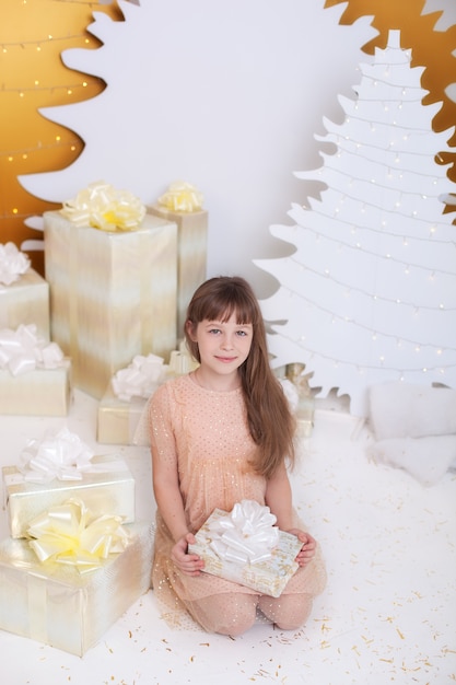 Conceito de férias de Natal. menina de vestido dourado, sentado junto à árvore de Natal com presente.