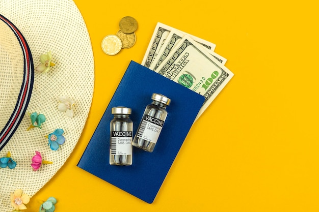 Conceito de férias de verão durante o passaporte de chapéu de palha pandêmico de coronavírus com dinheiro e frascos de vacina espaço de cópia de fundo amarelo plano foto