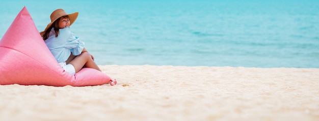 Conceito de férias de verão jovem mulher com vestido azul elegante e chapéu de palha com céu azul na praia.