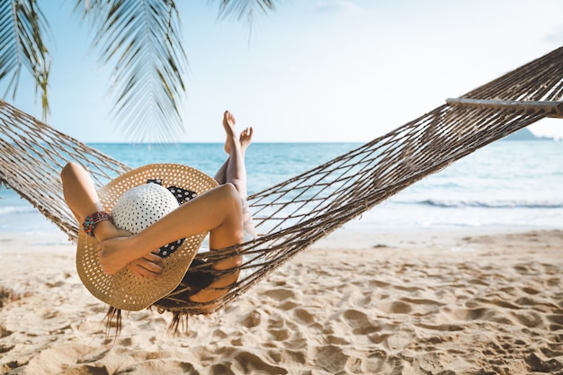 Foto conceito de férias de viagens de verão. mulher asiática feliz com biquíni branco relaxando em uma rede na praia em koh mak, tailândia