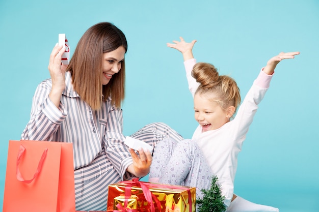 Conceito de férias em família. mãe e filha de pijama com presentes juntos, sentados no chão da sala azul.