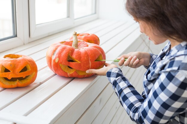 Conceito de férias, halloween, decoração e pessoas - close-up de uma mulher com abóboras se preparando para o halloween