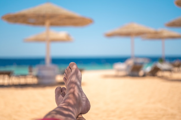 Conceito de férias homem pés descalços sobre o fundo do mar Férias de férias conceito de relaxamento pés na praia conceito de férias de verão Perspectiva pessoal do homem relaxante vista dos pés