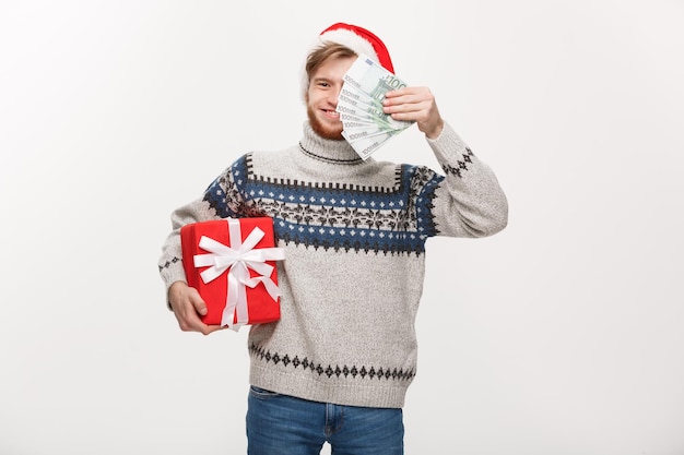 Conceito de férias jovem barbudo segurando uma caixa de presentes de natal e dinheiro sobre fundo branco