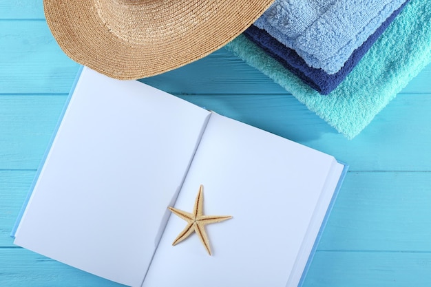 Conceito de férias Pilha de livro aberto de toalhas e chapéu na mesa de madeira azul