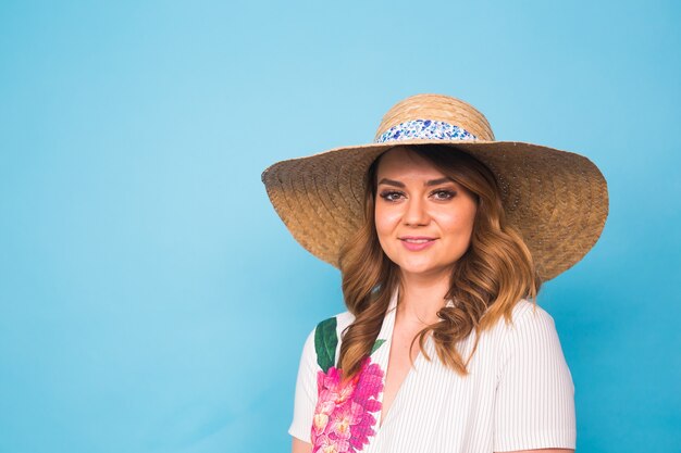 Conceito de férias, verão, moda e pessoas - garota com chapéu de palha de roupas da moda. retrato de uma mulher encantadora sobre fundo azul com espaço vazio da cópia.