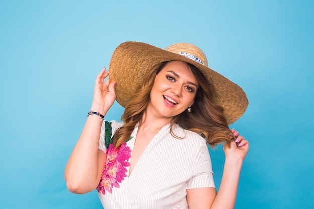 Conceito de férias, verão, moda e pessoas - garota com chapéu de palha de roupas da moda. Retrato de uma mulher encantadora sobre fundo azul com espaço vazio da cópia.