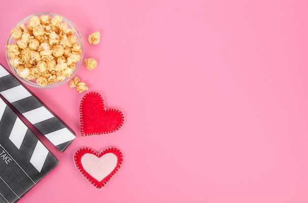 Conceito de filme do dia dos namorados. Claquete de filme com corações e pipoca de caramelo com espaço de cópia no fundo rosa.