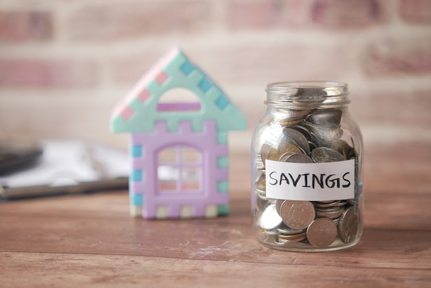 Conceito de finanças da casa com o modelo da casa e economizando o frasco de moedas na mesa