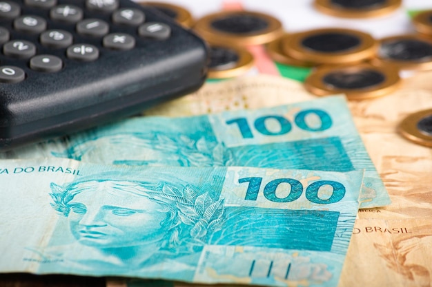 Foto conceito de finanças notas de cem reais com calculadora e moedas dinheiro brasileiro