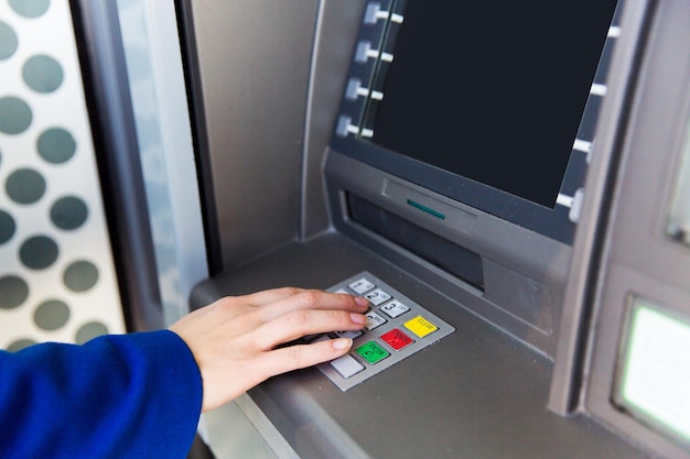 conceito de finanças, tecnologia, dinheiro e pessoas - close-up da mão inserindo o código PIN no caixa eletrônico