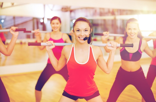 conceito de fitness, desporto, treino, ginásio e estilo de vida - treinador sorridente em frente ao grupo de pessoas que se exercitam com barras no ginásio