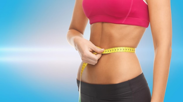 conceito de fitness, dieta e partes do corpo - close-up da barriga treinada com fita métrica