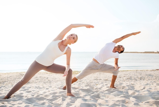 conceito de fitness, esporte, amizade e estilo de vida - casal fazendo exercícios de ioga na praia